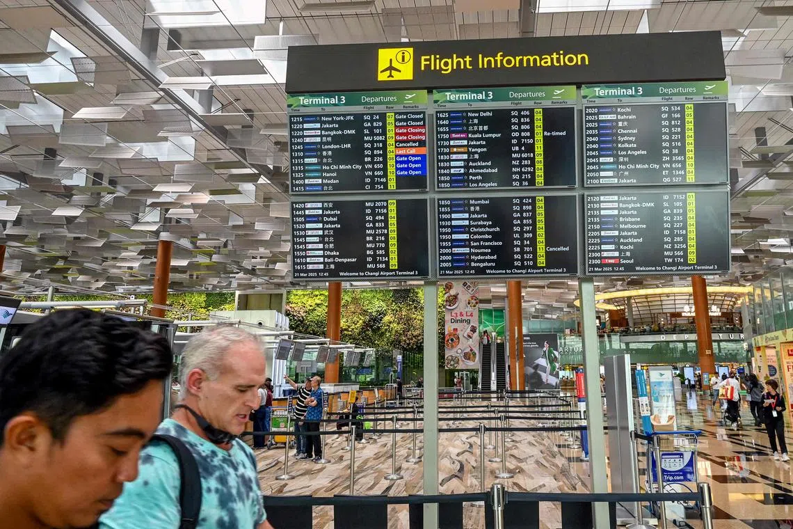 Travellers walk past a departure board at Singapore's Changi Airport on March 21.