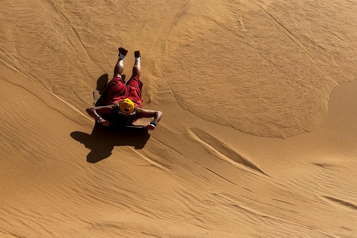 A tourist sandboards on the dunes in Walvis Bay, Namibia February 26, 2024. REUTERS/Shafiek Tassiem