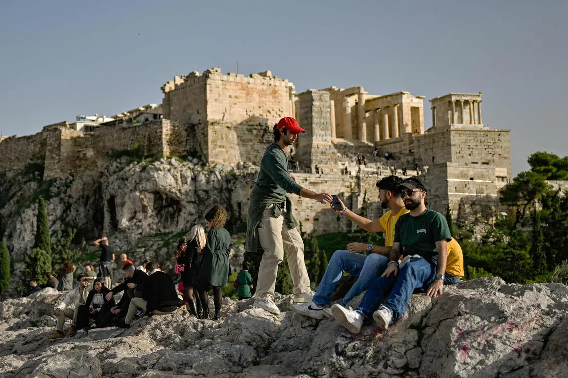 Tourists enjoy the Aeropagus Hill in Athens, beneath the Acropolis  on December 8, 2022. - With most of Europe's wary of soaring energy costs, Greece has launched an initiative to put its mild winters to good use in attracting travellers. (Photo by Louisa GOULIAMAKI / AFP)