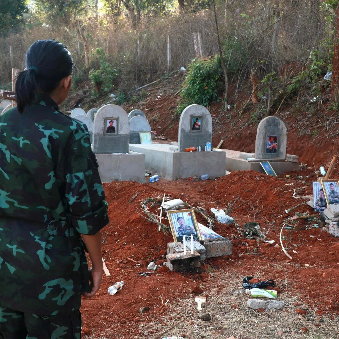 (FILES) This photo taken on March 6, 2025 shows an Urban Revolution Front (URF) soldier in front of gravestones of two URF soldiers killed by a Myanmar military drone attack in the forest near Moe Bye in Myanmar's eastern Shan State. More than 100,000 people have been killed across all sides in Myanmar since a military coup five years ago triggered civil war, a conflict monitor said July 1, 2026. (Photo by AFP)