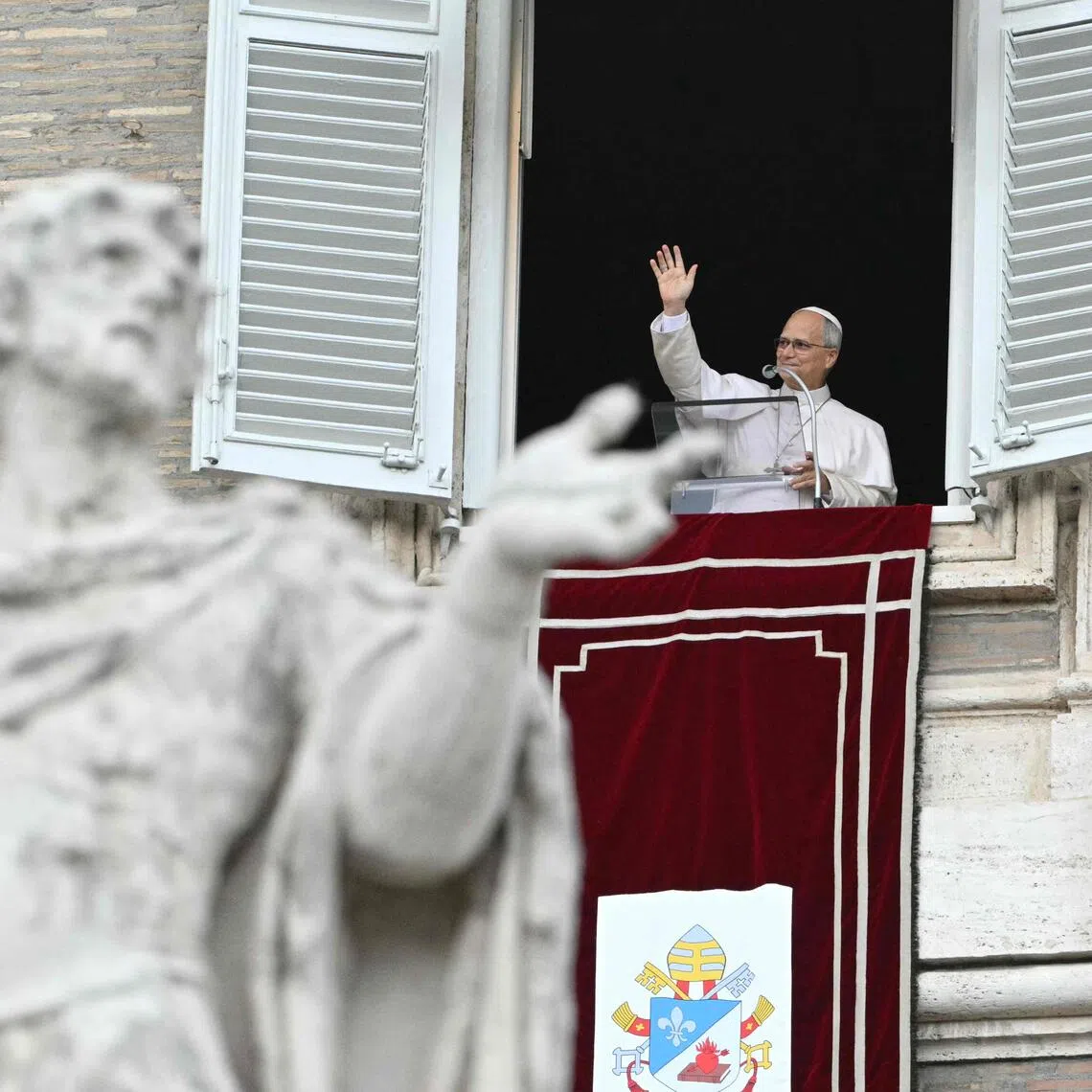 Pope Leo waves from the window of the apostolic palace overlooking St. Peter’s square during the Angelus prayer on Oct 18.