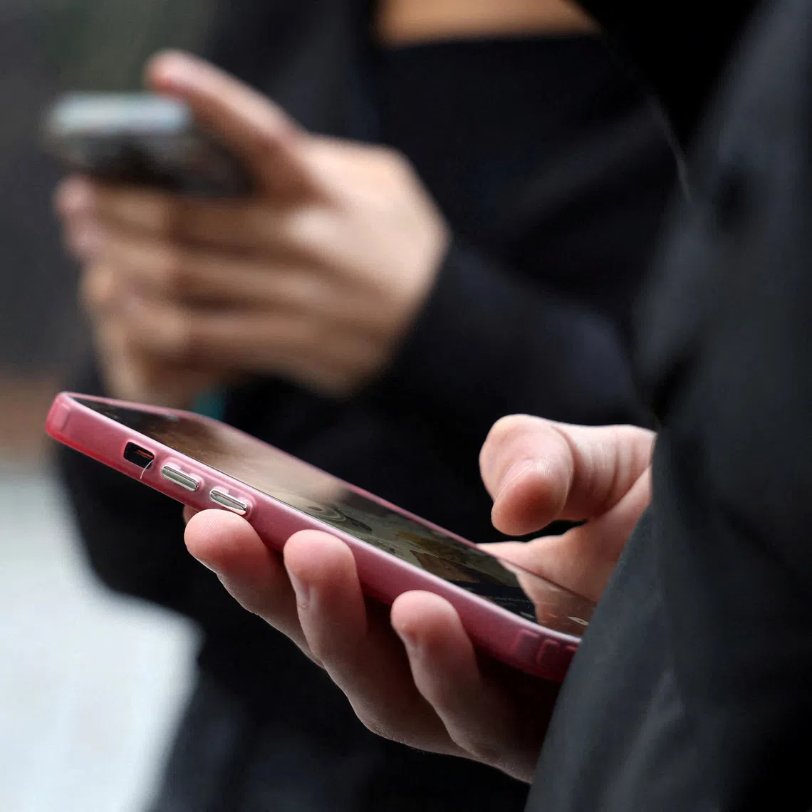 FILE PHOTO: Teenagers look at their mobile phone screens during an interview with Reuters about the bill aimed at banning the use of social networks for those under 15 and mobile phones in high schools from the start of the 2026 school year, in Paris, France, February 20, 2026. REUTERS/Manuel Ausloos/File Photo