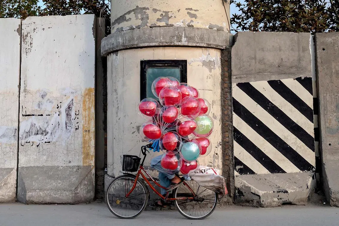 TOPSHOT - An Afghan balloon vendor rides past the blast wall along a street in Kabul on October 16, 2024. (Photo by Wakil KOHSAR / AFP)