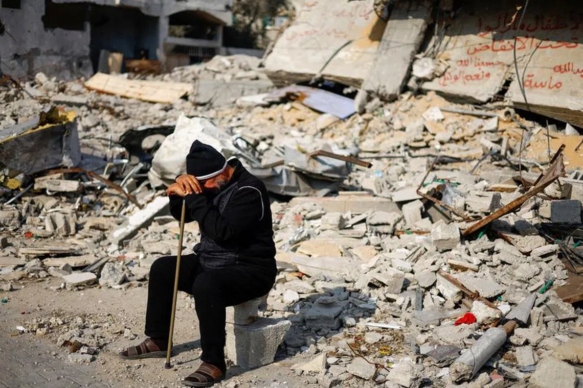Ziad Mansour, a neighbour of the Abu Aweidah family, sits next to writing painted on a wall amid the rubble of the family's house, which was destroyed in a deadly Israeli strike amid the ongoing conflict between Israel and the Palestinian Islamist group Hamas, in Rafah, Gaza Strip, January 9, 2024. REUTERS/Mohammed Salem
