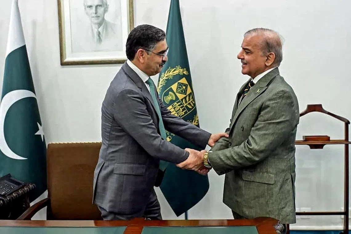 Interim Prime Minister Anwaar-ul-Haq Kakar  (left) and outgoing Prime Minister Shehbaz Sharif shake hands at the President House in Islamabad. 