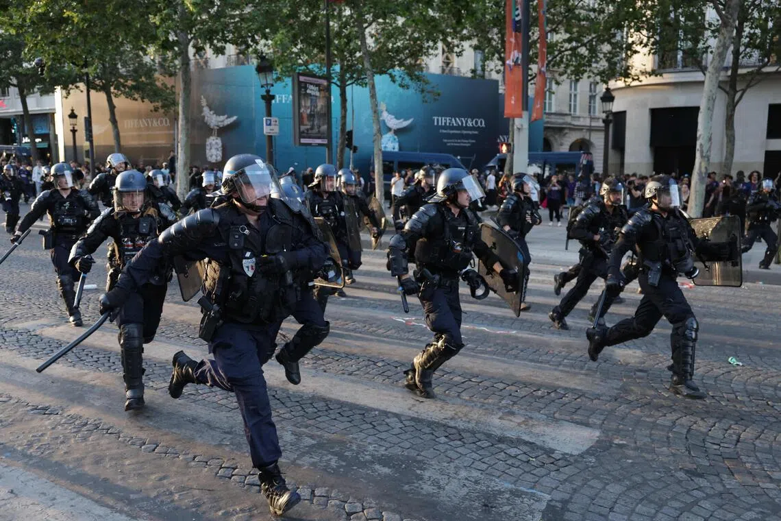 Police officers run to disperse PSG supporters on the Champs-Elysees Avenue during the Champions League final.