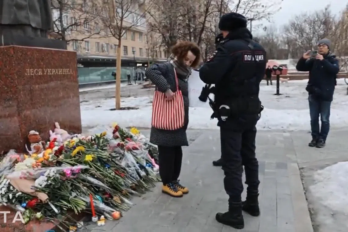 Russian police step in to arrest a woman after she briefly held up a sign at a monument in Moscow in support of Ukraine, in a screenshot from video footage posted online.