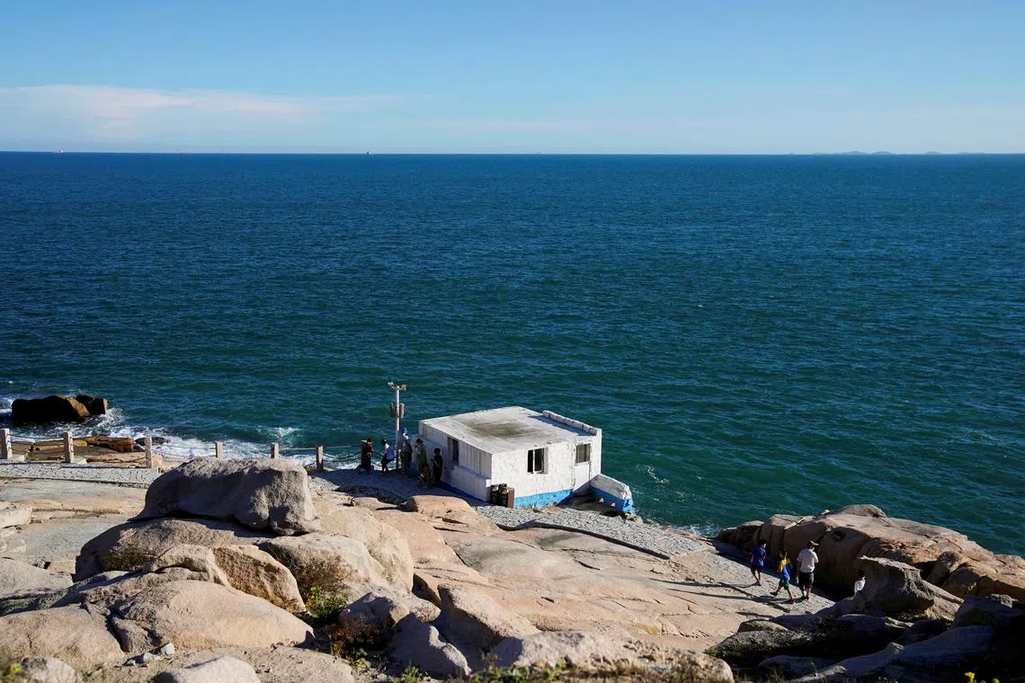FILE PHOTO: People stand near a building overlooking the Taiwan Strait, at the 68-nautical-mile scenic spot, one of mainland China's closest points to the island of Taiwan, in Pingtan island, Fujian province, China August 5, 2022. REUTERS/Aly Song/File Photo