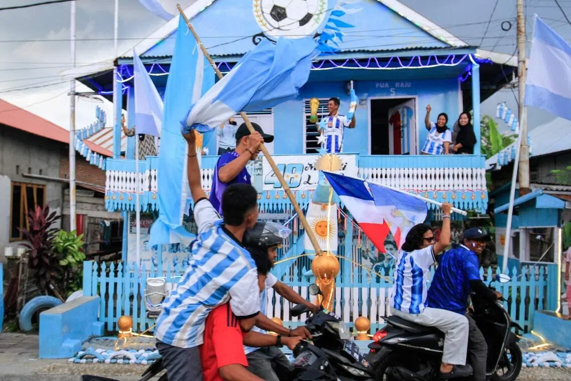 Argentina and Lionel Messi fan Muhammad Yusuf holds a replica of the World Cup trophy as football fans pass his house, painted in the colours of the Argentine flag.