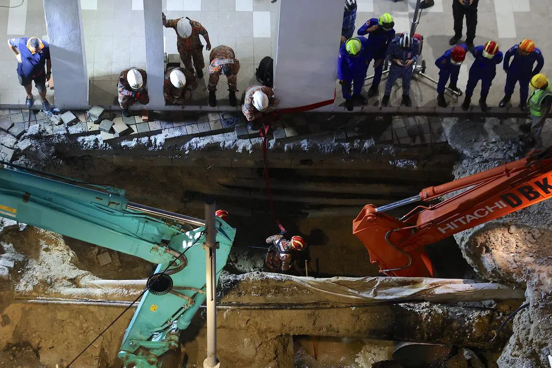 Malaysia Fire and Rescue Department officers inspect the site where a woman fell into an eight-metre deep sinkhole in Kuala Lumpur.
