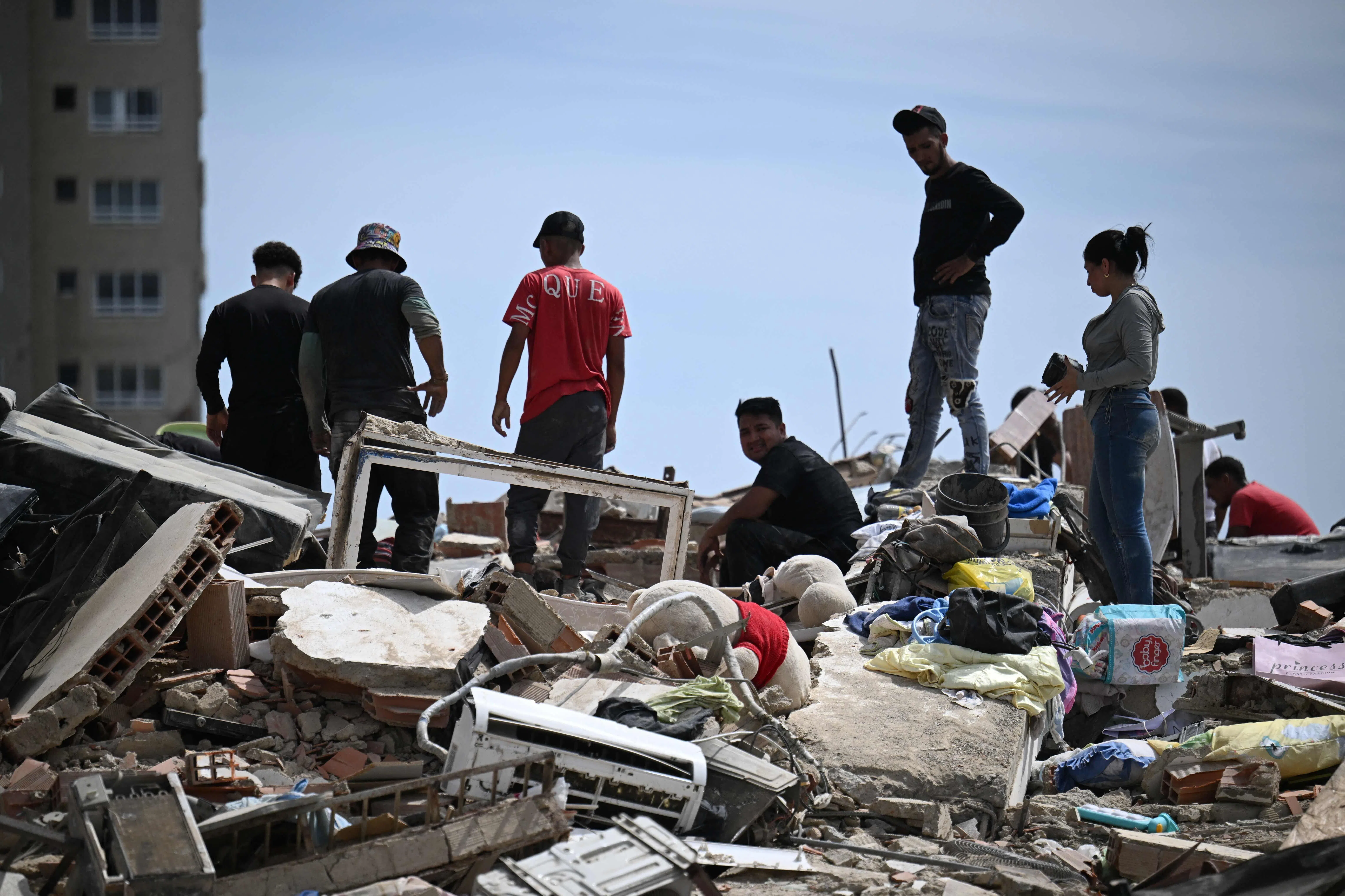 Residents search through the rubble of collapsed buildings as they try to recover belongings following an earthquake in Catia La Mar, La Guaira state, about 30 km northwest of Caracas, on June 25, 2026. A twin earthquake that was Venezuela's largest in over a century has killed at least 164 people and destroyed multiple buildings near the capital, where residents searched on June 25 for missing relatives. (Photo by Juan BARRETO / AFP)
