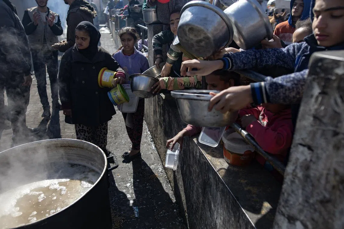 Displaced Palestinians hold empty pots and buckets as they line up to receive food aid at Rafah refugee camp, southern Gaza Strip, on Feb 1.