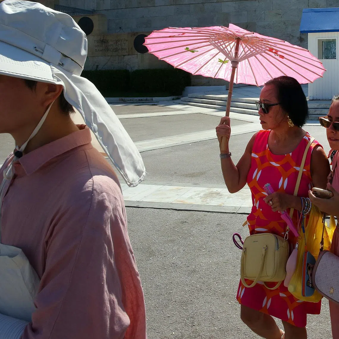 Tourists wear hats and use fans and umbrellas as they stroll in the city centre during a heatwave in Athens, Greece.