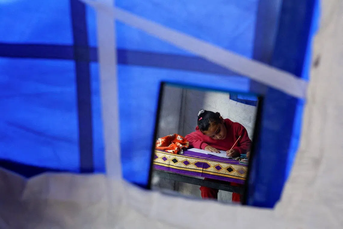 Displaced Palestinian girl Toulin Al-Hindi, 7, is reflected in a hanging mirror as she does her homework inside her family's tent near the Israeli-designated \"yellow line\", in Beit Lahiya, northern Gaza Strip, January 6, 2026. REUTERS/Mahmoud Issa