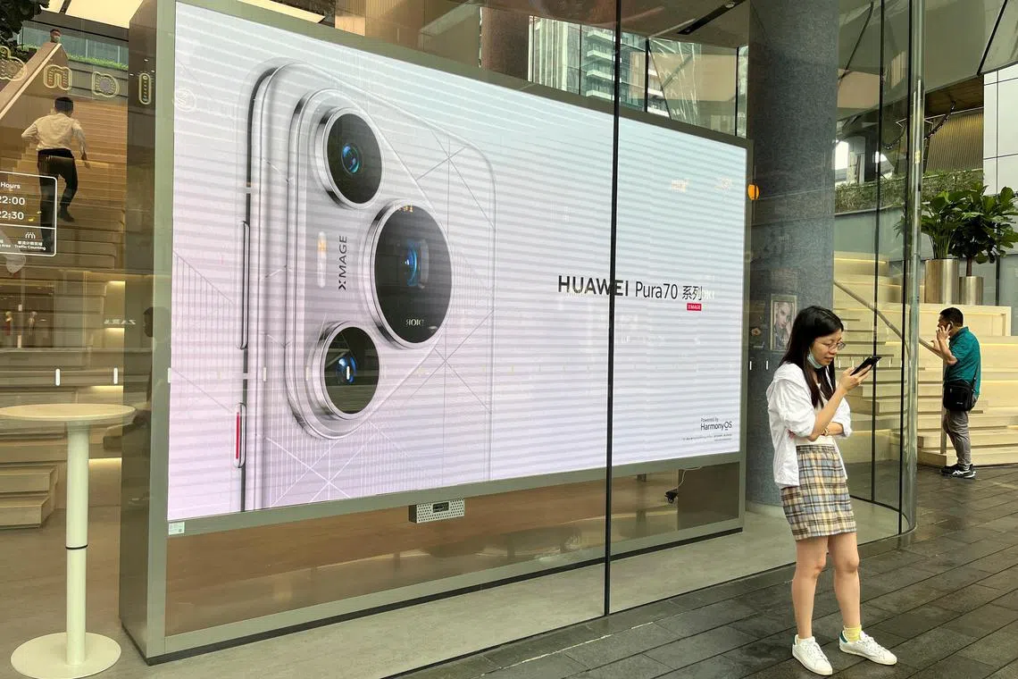 A woman uses her cellphone while standing in front of a screen advertising Huawei Pura 70 series smartphones outside Huawei's flagship store in Shenzhen, China April 26, 2024. REUTERS/David Kirton
