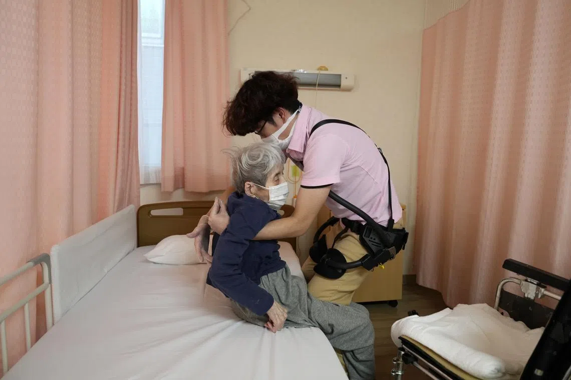 A staff member wearing a Laevo exoskeleton transferring an elderly resident back to her bed at the Shintomi nursing home in Tokyo, Japan on Oct 3, 2023.
