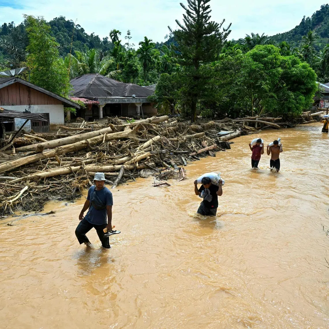 People wade through the floodwater in the aftermath of flash floods at Tukka village, North Sumatra province, on Dec 2.