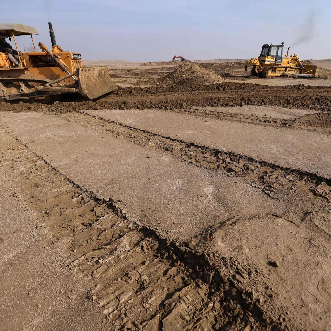 Bulldozers clear sand dunes and extract clay in the desert south of Samawah.