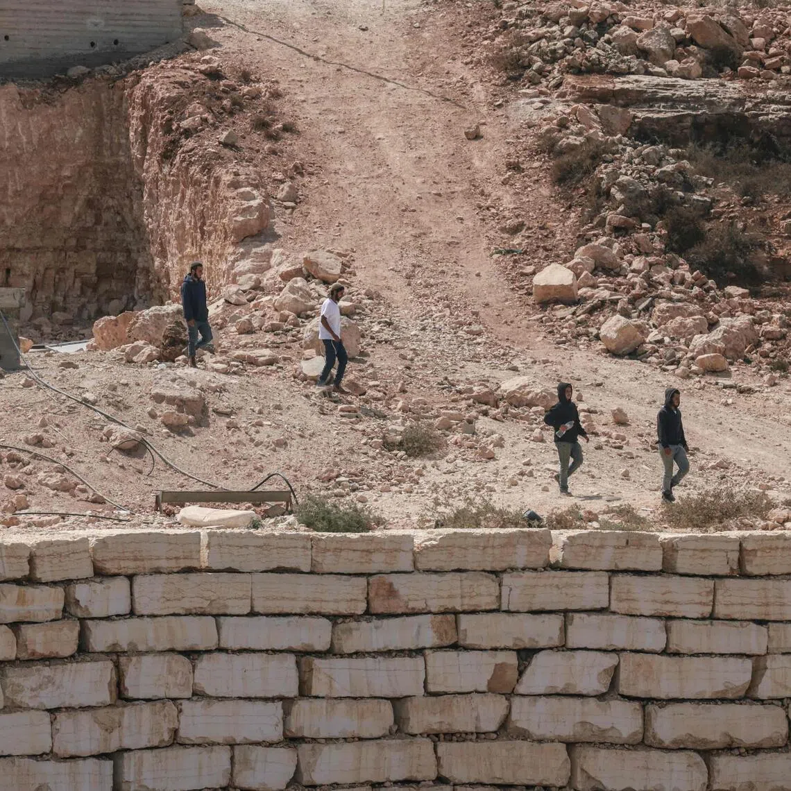 Israeli settlers walks towards a Palestinian home under construction in the village of Qusra, in the Israeli-occupied West Bank, which has faced escalating settler violence over the past month.