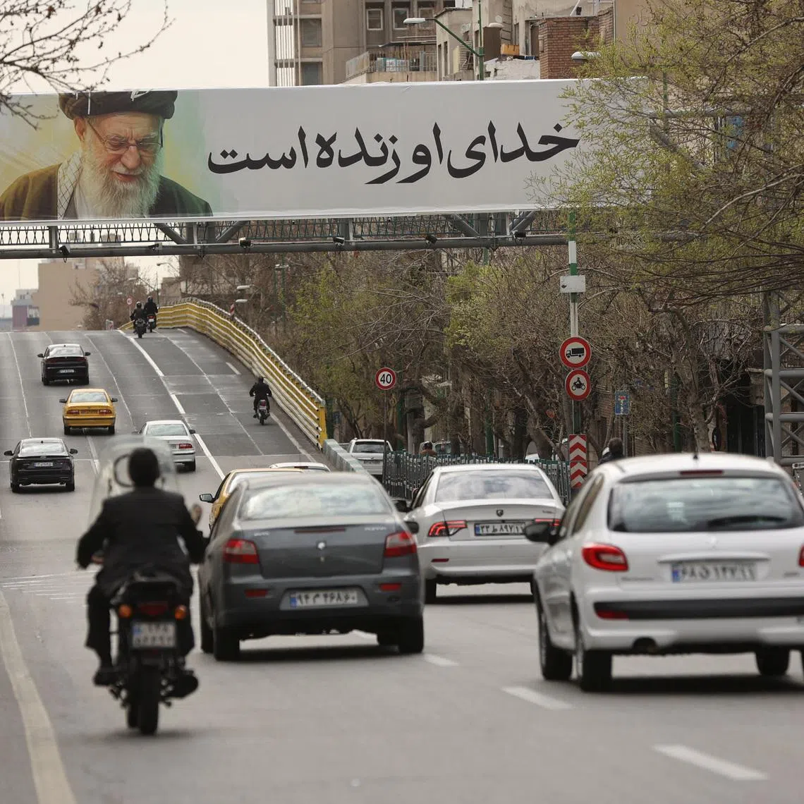 People drive near a banner of Iran's late Supreme Leader Ayatollah Ali Khamenei on a street, after he was killed in Israeli and U.S. strikes on Saturday, in Tehran, Iran, March 2, 2026. Majid Asgaripour/WANA (West Asia News Agency) via REUTERS