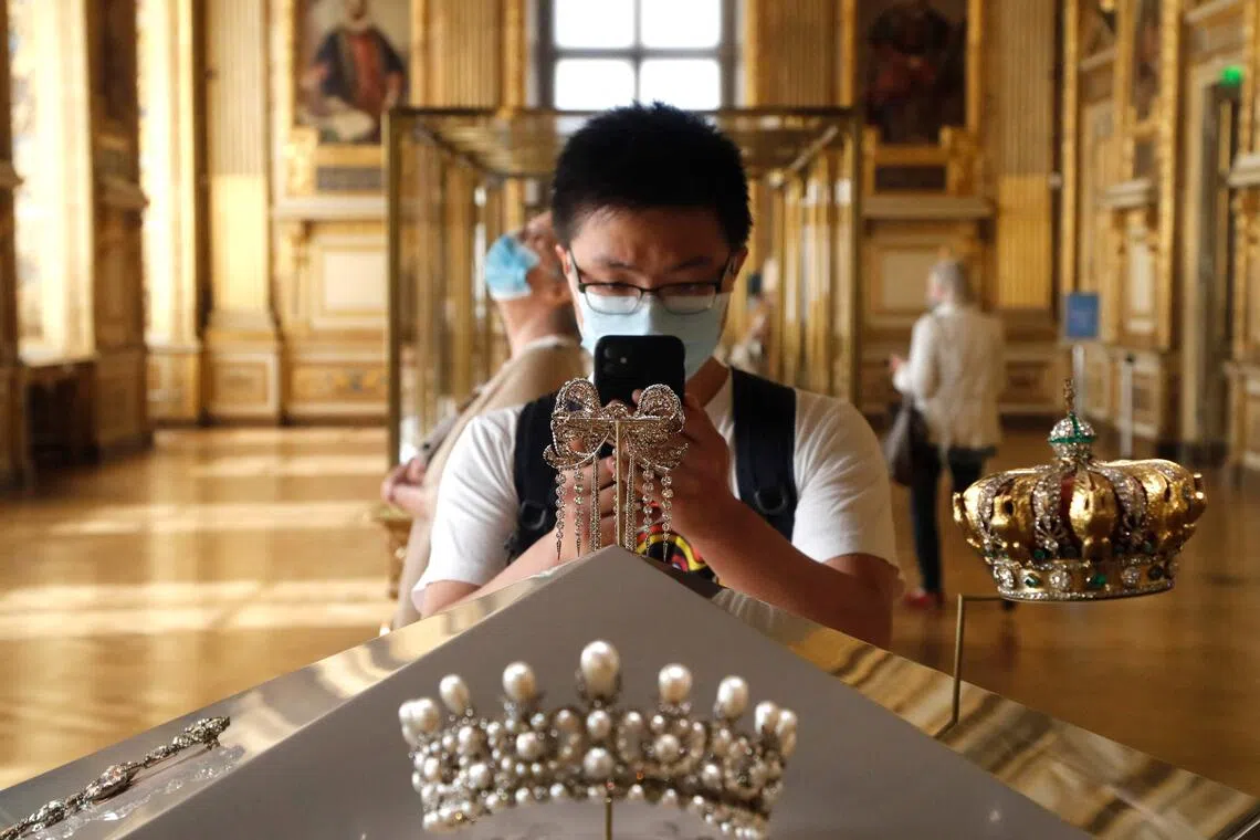 A 2020 photo shows a visitor taking photos of jewelled items worn by Empress Eugenie, including a tiara (front) and crown (right. The crown was dropped by the thieves during an Oct 19 heist at the Louvre. 