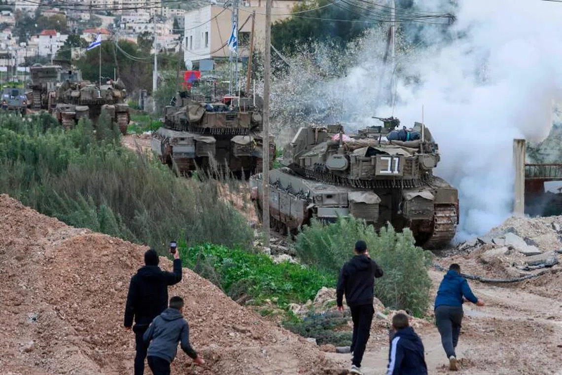Palestinian youths throw stones and film Israeli tanks and bulldozers entering the Jenin camp for Palestinian refugees in the occupied West Bank, on February 23, 2025. Israel on February 23 said troops would stay in West Bank refugee camps for the coming year, announcing expanded military operations including tank deployments, after the displacement of tens of thousands of Palestinians. (Photo by Jaafar ASHTIYEH / AFP)