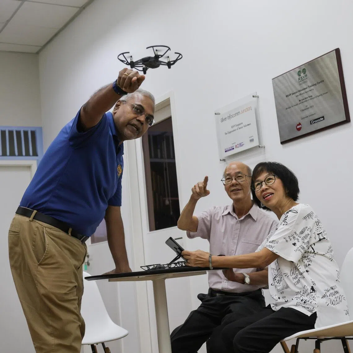 Santhanam Srinivasan, (left) an RSVP Singapore volunteer, shows Leong Wing Sun and Sheila Lim how to operate a drone.