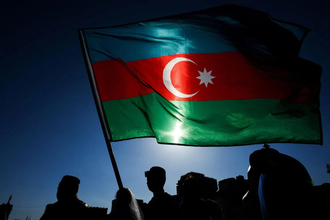 (FILES) Schoolchildren wearing traditional dresses wave an Azerbaijani flag during the annual Day of Reading event outside the Heydar Aliyev Cultural Center in Baku on April 26, 2018. Azerbaijani President Ilham Aliyev on December 7, 2023 called snap presidential elections in February, in a move expected to further extend the decades-long authoritarian rule of his family. (Photo by Kirill KUDRYAVTSEV / AFP)