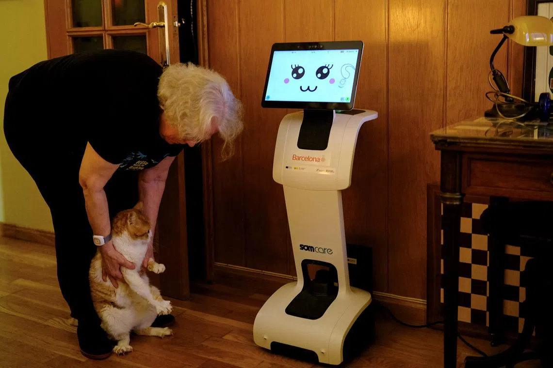 Irene Veglison, 67, holds her cat named Sweet, net to her robot, nicknamed \"Sandi\", inside her apartment, where she lives with two cats and her robot, during a pilot project to improve tele-assistance, to provide support to those experiencing the early stages of cognitive decline, in Barcelona, Spain, February 26, 2026. REUTERS/Nacho Doce