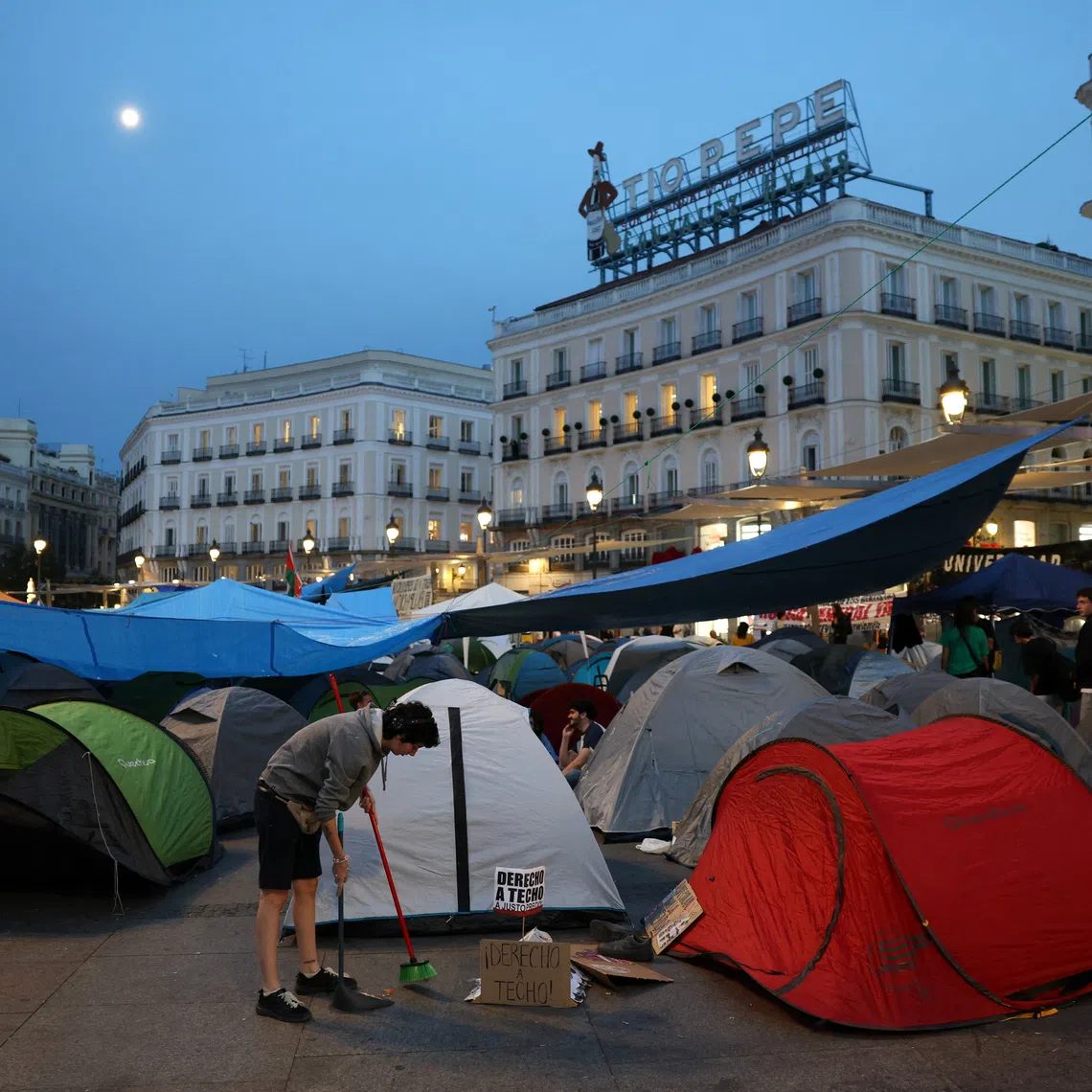 A protester sweeps the pavement next to a sign that reads \"Right to housing\" after demonstrators set up a tent camp at Puerta del Sol square in protest against Spain's housing crisis after the forceful eviction of an 87-year-old woman from her apartment in Madrid, Spain, September 28, 2026. REUTERS/Juan Medina