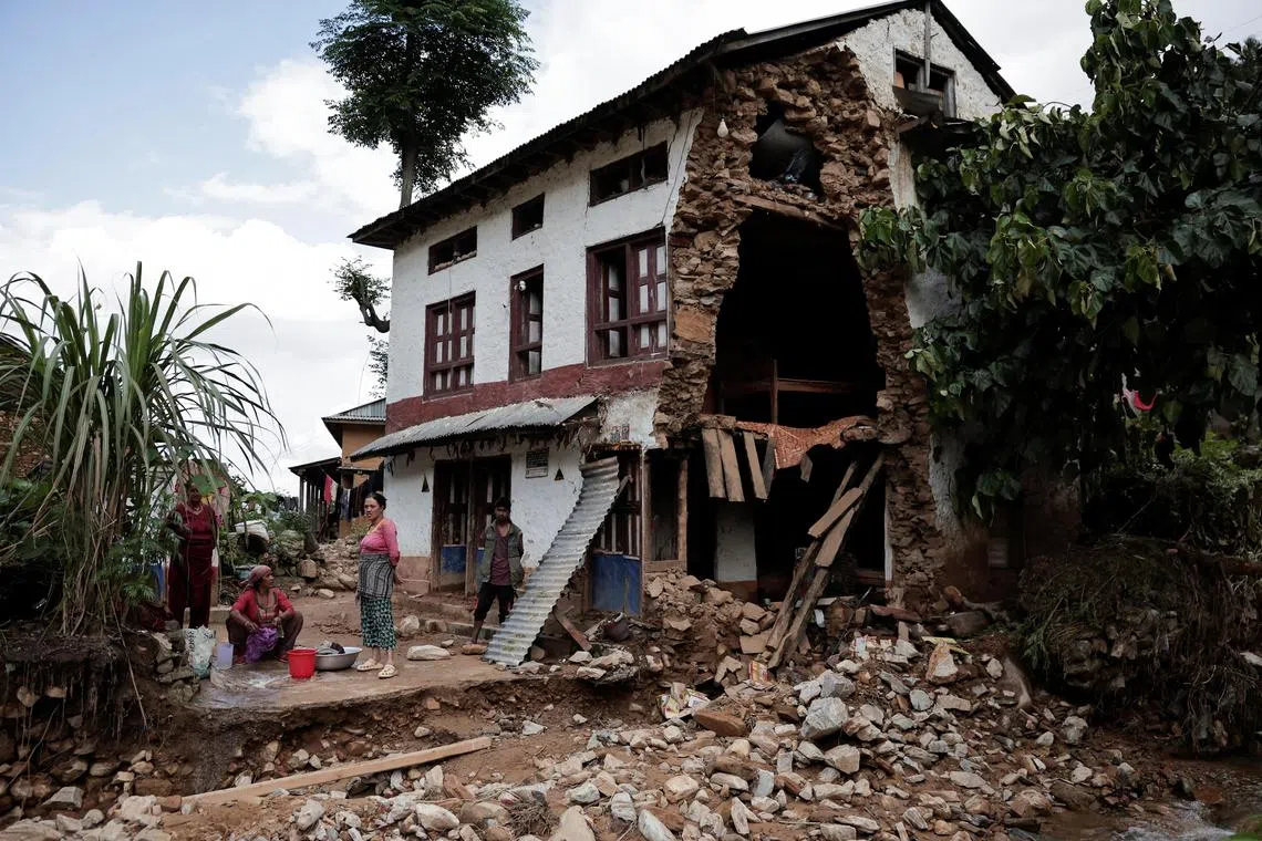 People stand in front of a partially damaged house after the deadly flood following heavy rainfall along the bank of Roshi River in Nepal on Sept 30.