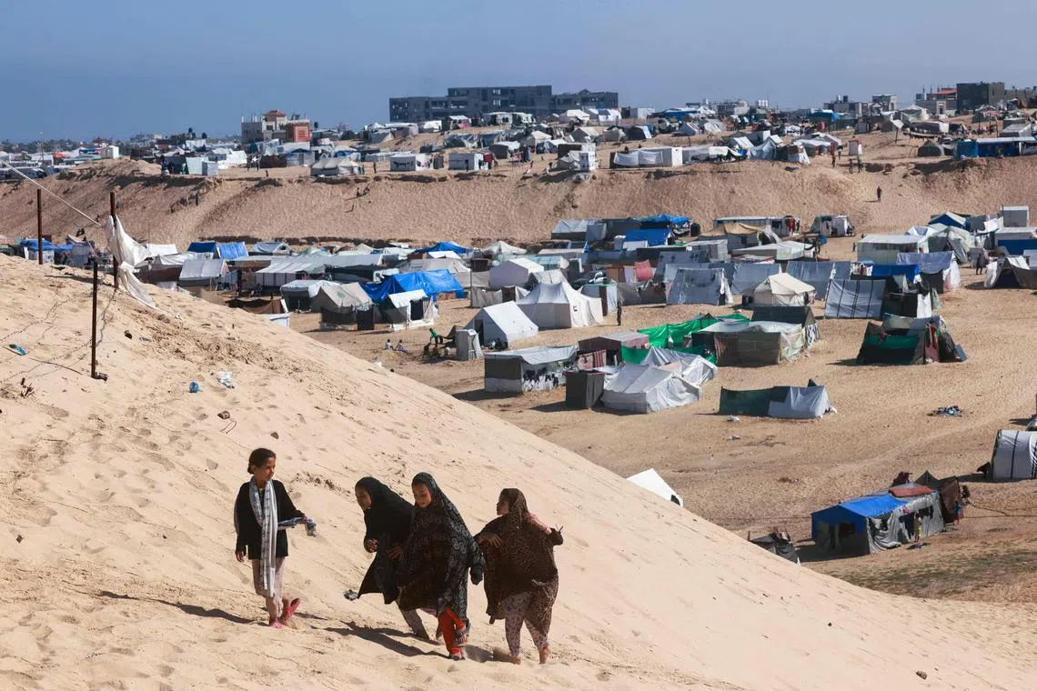 Palestinian girls walking up a sandy hill next to a makeshift tent camp for displaced people in Rafah in the southern Gaza Strip on April 4, 2024.