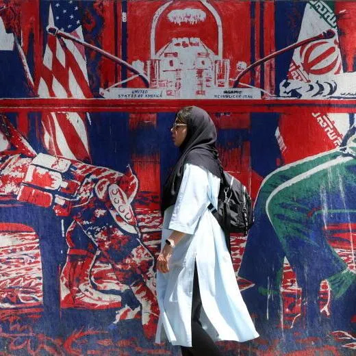 An Iranian woman walking past a mural depicting an Iranian and US negotiation table next to the former US embassy in Tehran.