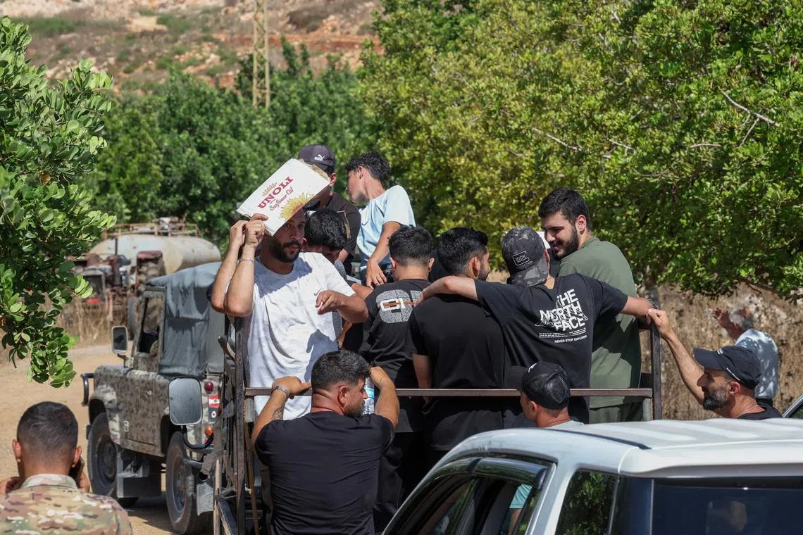 A man shields himself from the sun as residents wait to enter the town of Zawtar al-Gharbiyeh, following the withdrawal of Israeli forces under a U.S.-brokered plan, next to Lebanese soldiers, in southern Lebanon, July 24, 2026. REUTERS/Aziz Taher