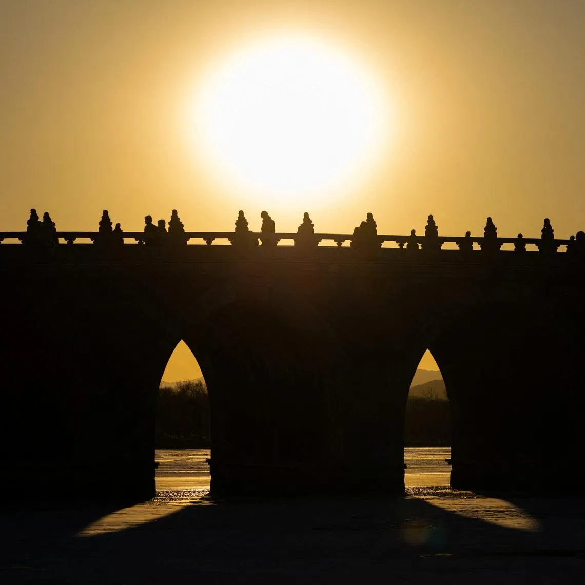 People walk on Seventeen-Arch Bridge, also known as Shiqikong Qiao, as the sun sets at Summer Palace in Beijing, China, on Jan 20.