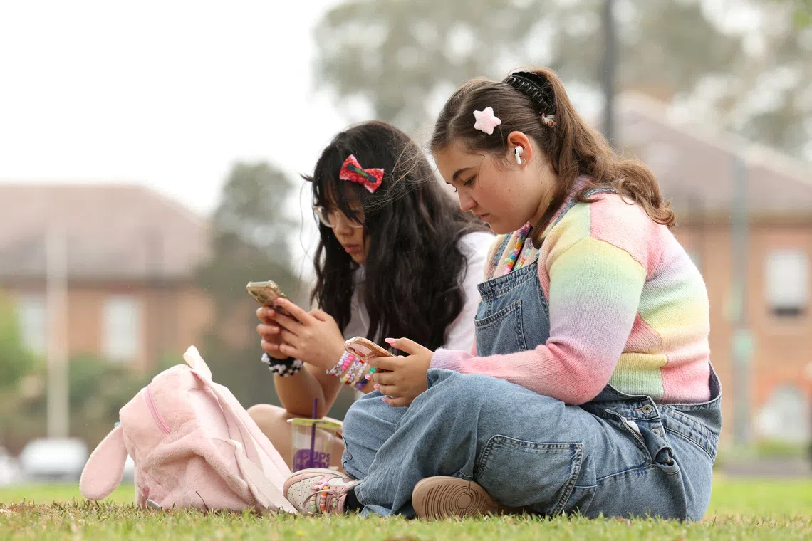 Annie Wang, 14, and Ayris Tolson, 15, use their mobile phones, ahead of Australia’s social media ban for users under 16, which is scheduled to take effect on December 10, in Sydney, Australia, November 22, 2025. REUTERS/Hollie Adams