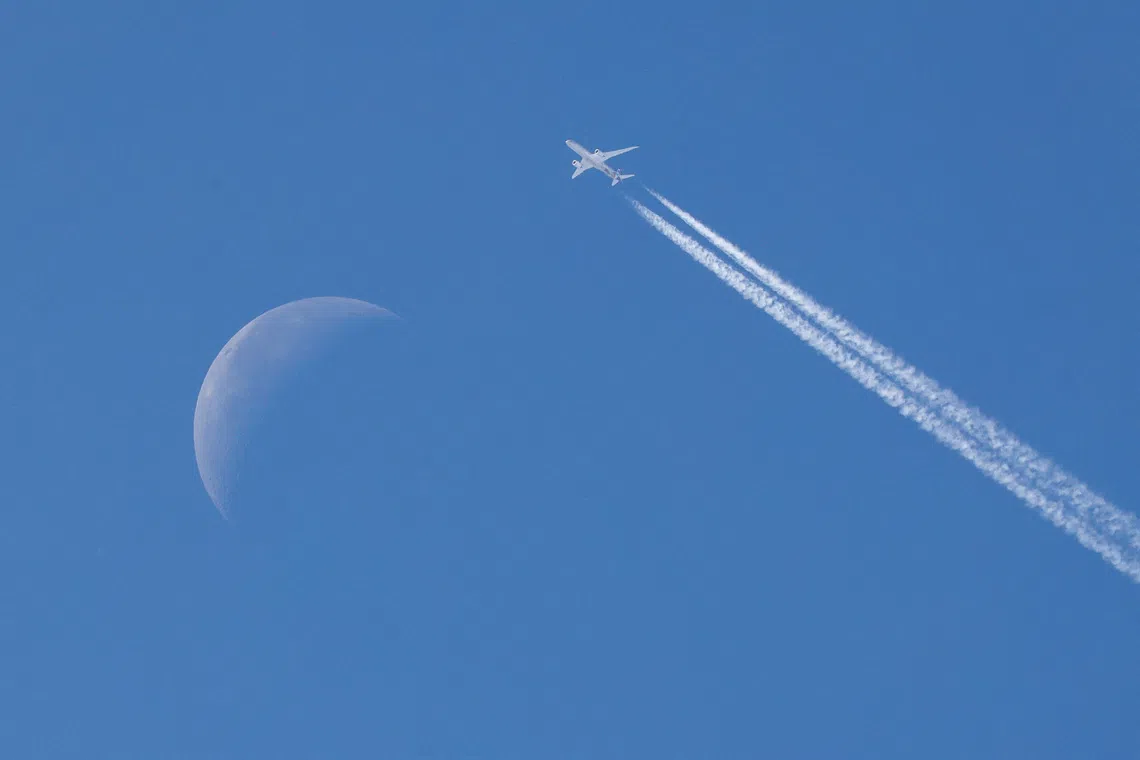A passenger plane flying through the sky with the moon in the background over Belgrade, Serbia, on Sept 16, 2025. 