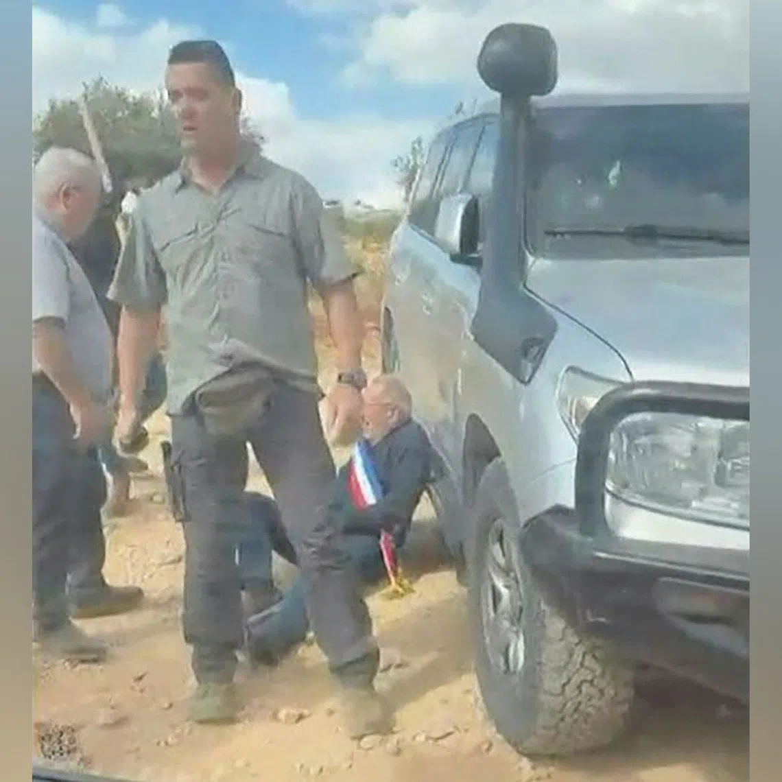 A man wearing a blue, white and red sash, of the type used by French public officials, leaning against a vehicle as men intercept and surround a car carrying activists in the Christian village of Taybeh, in the Israeli-occupied West Bank.