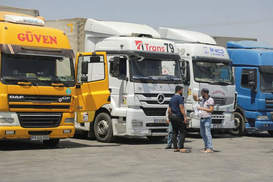 FILE PHOTO: People stand near trucks parked at Bab al-Salameh border crossing in Aleppo countryside, Syria August 9, 2023. REUTERS/Mahmoud Hassano/File Photo