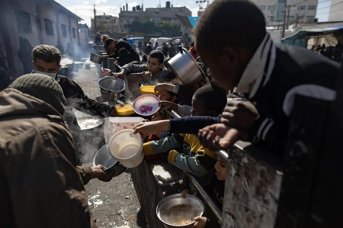 Displaced Palestinians hold empty pots and buckets as they line up to receive food aid at a refugee camp in Rafah.