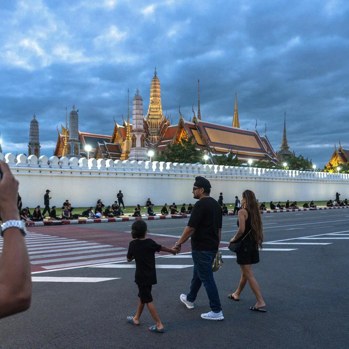 A family dressed in black crosses a street in front of the Grand Palace in Bangkok on Oct 26, 2025.