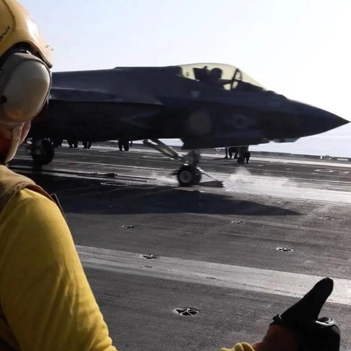 A flight deck crew member signals an F‑35 jet taking off from a US aircraft carrier during operations against Iran.
