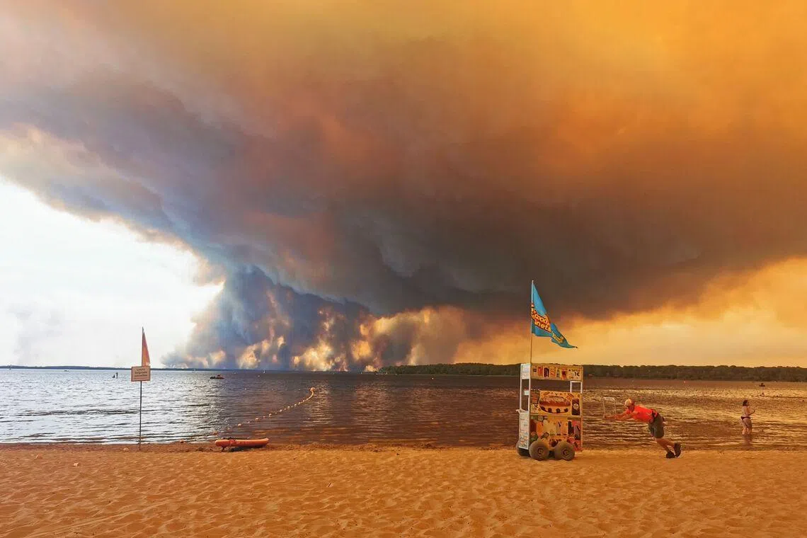 A vendor pushes a cart on the beach of Moutchic in Lacanau, southwestern France on July 24, as clouds of smoke rise into the sky from a wildfire.