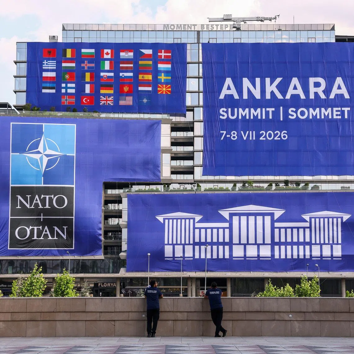 People stand near banners displaying logos and flags, on the sidelines of the NATO leaders' Summit in Ankara, Turkey, July 7, 2026. REUTERS/Yves Herman