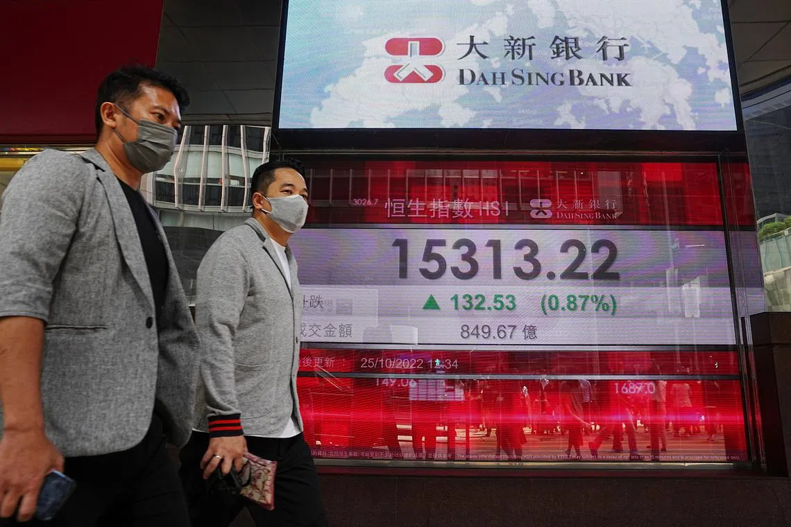 People walk past a screen displaying the Hang Seng stock index at Central district, in Hong Kong.