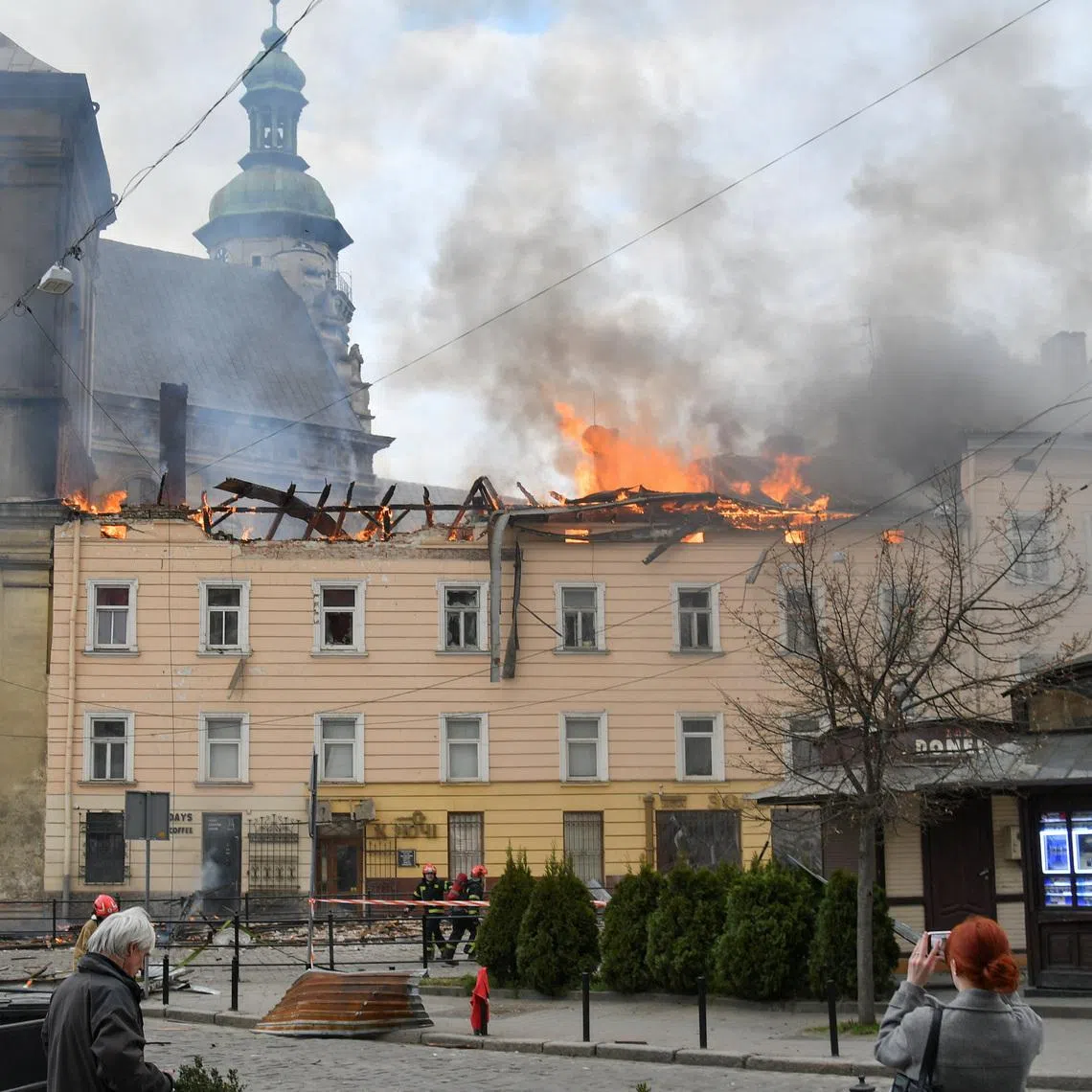 Residents look at firefighters who work at the site of a building which was hit by a Russian drone strike, amid Russia's attack on Ukraine, in the downtown of Lviv, Ukraine, March 24, 2026. REUTERS/Stringer