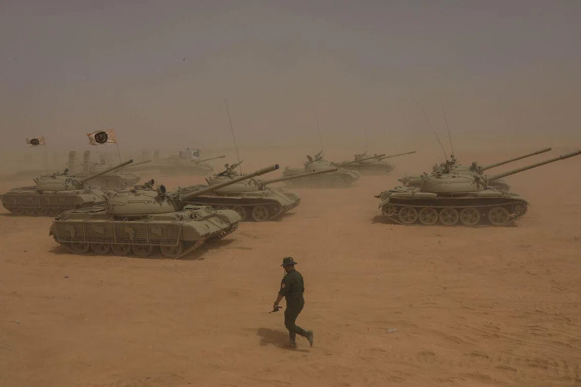 A Libyan soldier walking past some tanks during the "Dara al-Karama 2" military exercises, conducted by the Libyan National Army (LNA), under the command of Field Marshal Khalifa Haftar, in the Ras al-Alba region in southeastern Libya on May 16, 2026. 