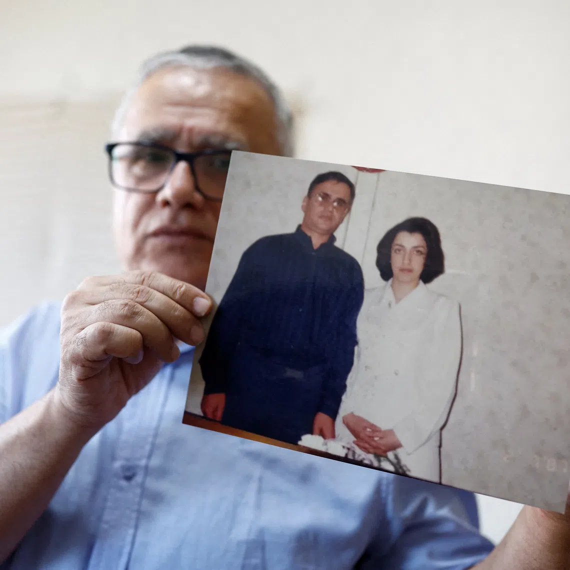 FILE PHOTO: Taghi Ramahi, husband of Narges Mohammadi, a jailed Iranian women's rights advocate, who won the 2023 Nobel Peace Prize, poses with an undated photo of himself and his wife, during an interview at his home in Paris, France, October 6, 2023. REUTERS/Christian Hartmann/File Photo