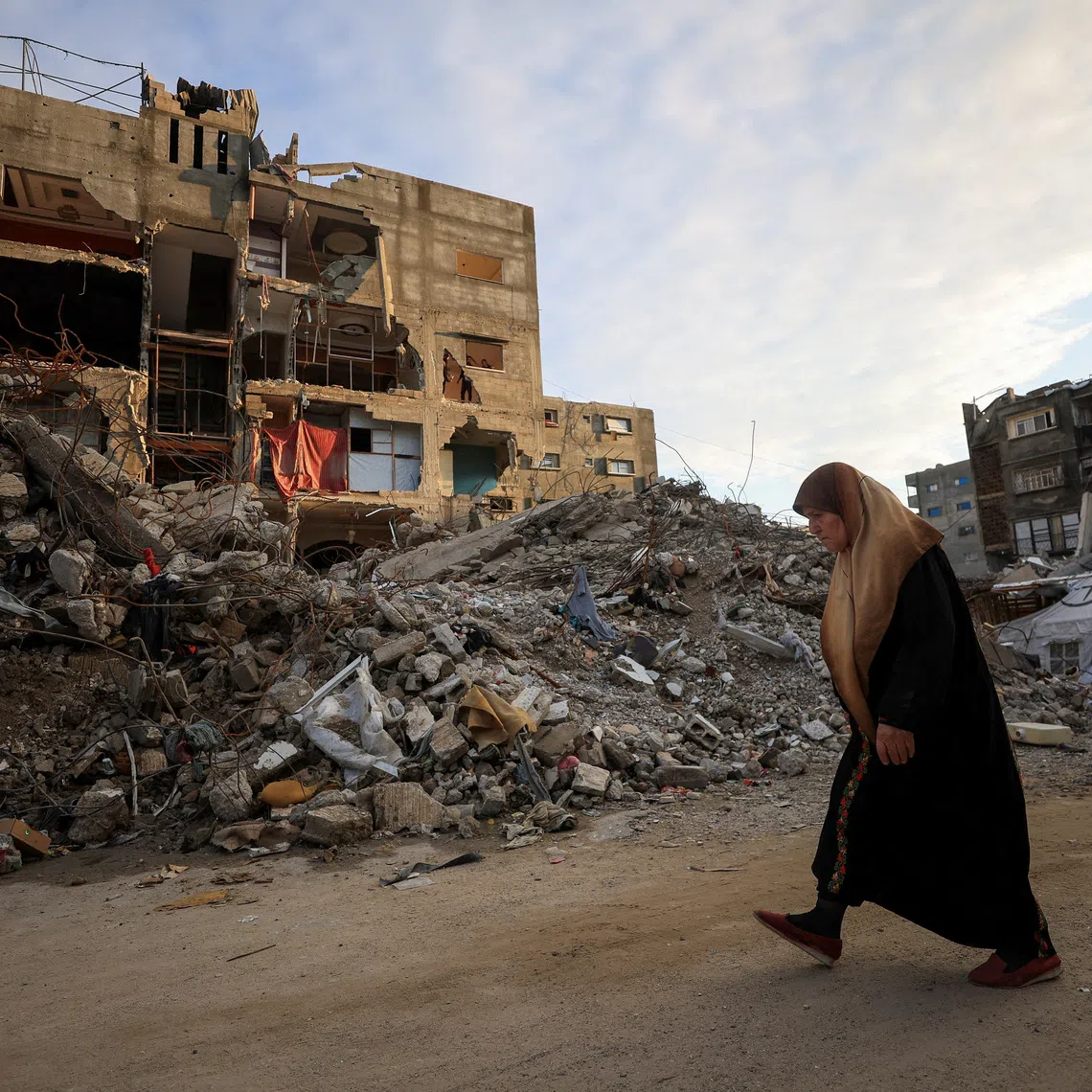 FILE PHOTO: A Palestinian woman walks past residential buildings damaged and destroyed during the war, in Gaza City, December 14, 2025. REUTERS/Dawoud Abu Alkas/File Photo