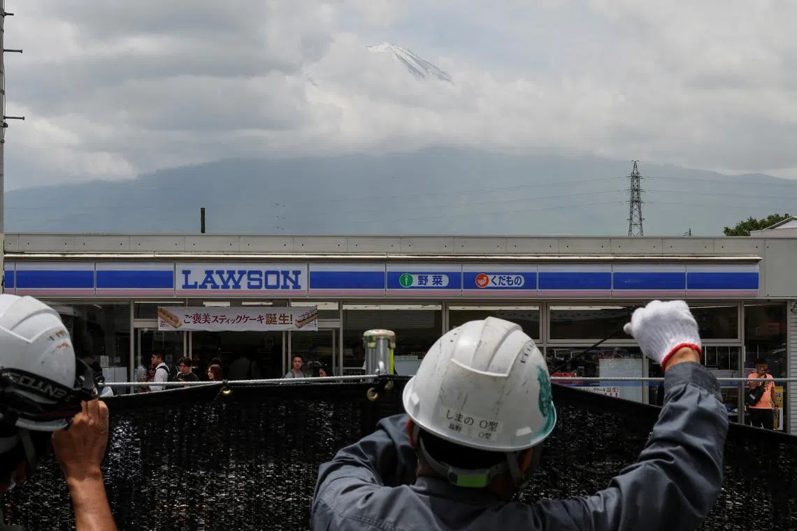 Workers erect a barrier to block the view of a popular Mount Fuji photo spot, near a convenience store in Fujikawaguchiko town, Yamanashi prefecture, Japan, May 21, 2024.   REUTERS/Kim Kyung-Hoon